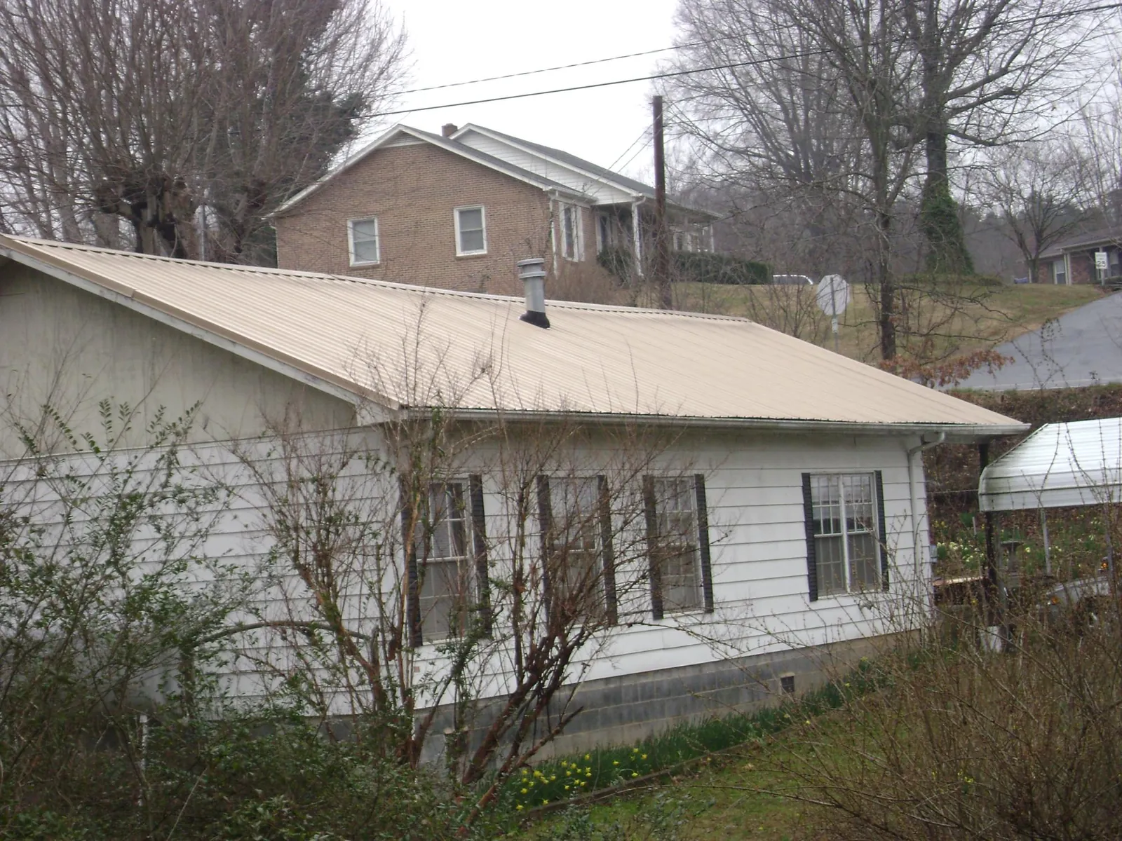 Tan metal roof on a white sided house set into a hillside — Commercial Roofing by Roofing Brothers in Trenton